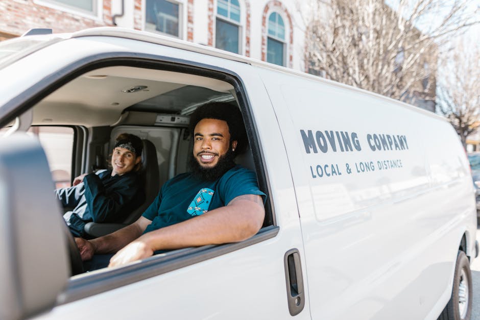 A photograph shows the interior view of a white moving van with the sliding door open, revealing two smiling individuals seated inside, one male with a beard wearing a navy blue T-shirt and the other